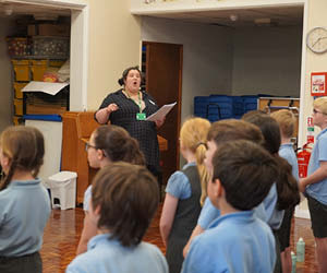 A woman singing in a room with schoolchildren.