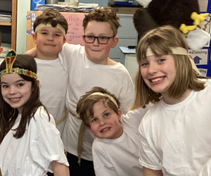 A group of smiling schoolchildren dressed in white clothes and gold headbands.