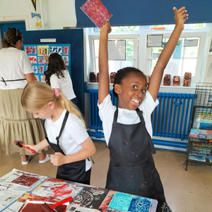 Two schoolchildren in aprons enjoying a print activity