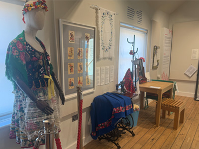 Mannequin in traditional Polish clothing and framed art and embroidery on the walls.