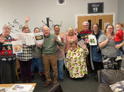 A group of people smile and wave for the camera in a community hall